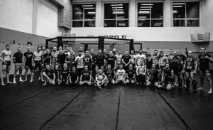 Grupa zawodników i trenerów Silesian Cage Club pozujących razem po treningu MMA w sali treningowej z klatką.